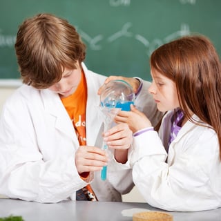 Young boy and girl in school learning chemistry working together as a team pouring liquids through a funnel into a test tube.jpeg